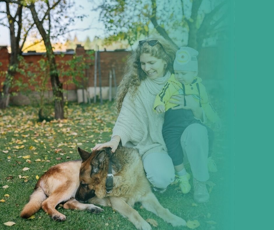 Photographie d'un berger allemand allongé au côté d'une femme et de son jeune enfant.